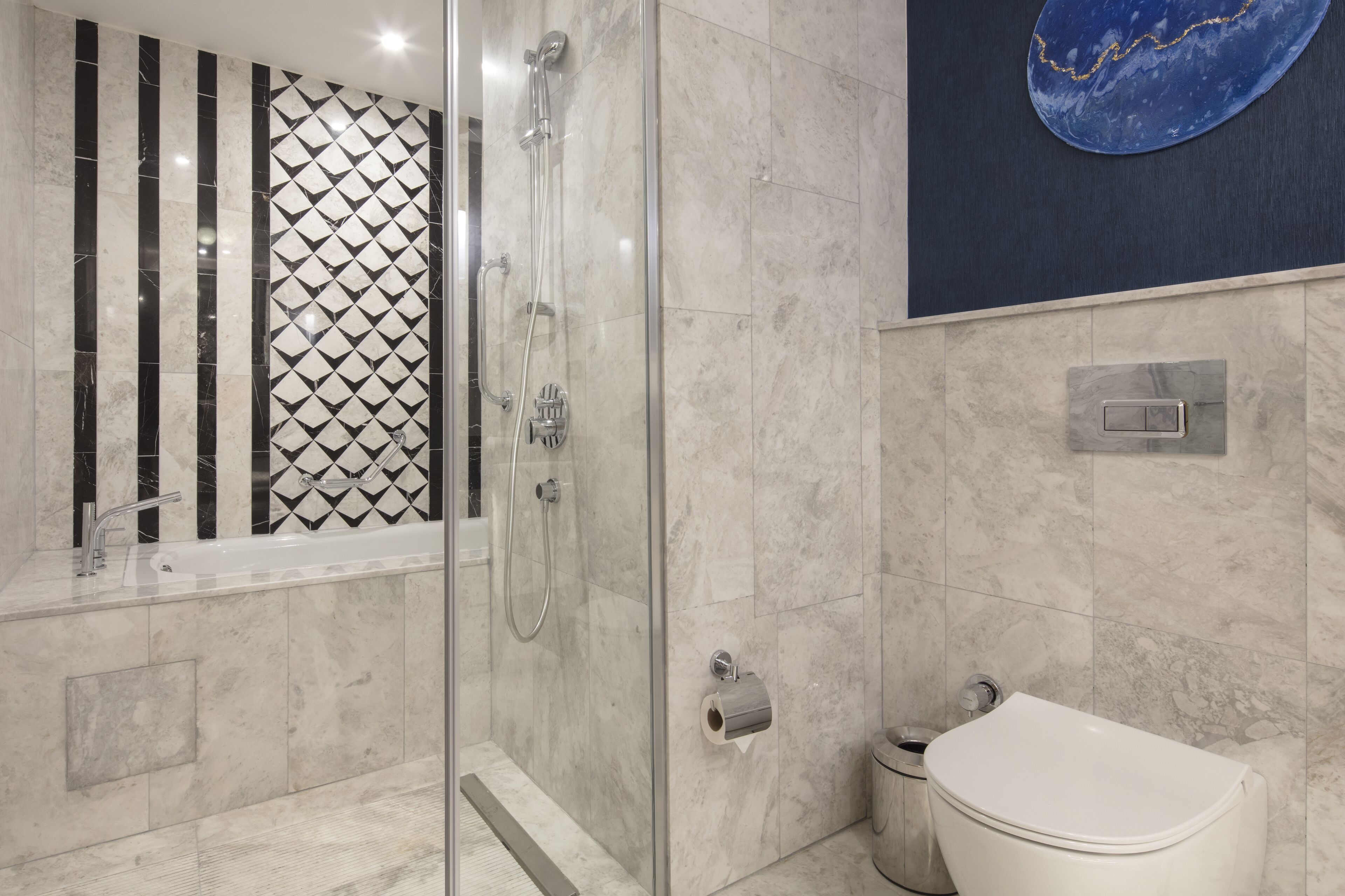 A modern bathroom with a glass-enclosed shower, a white sink, and a marble-tiled wall.