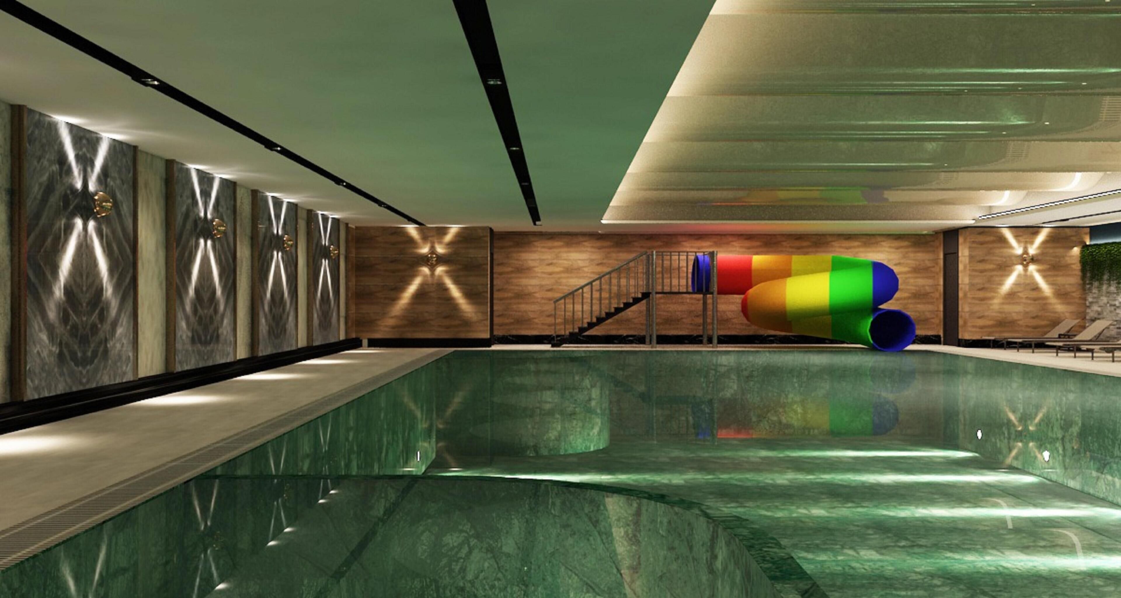 A modern indoor swimming pool with a colorful slide, a wooden wall with geometric patterns, and a staircase leading to a balcony.
