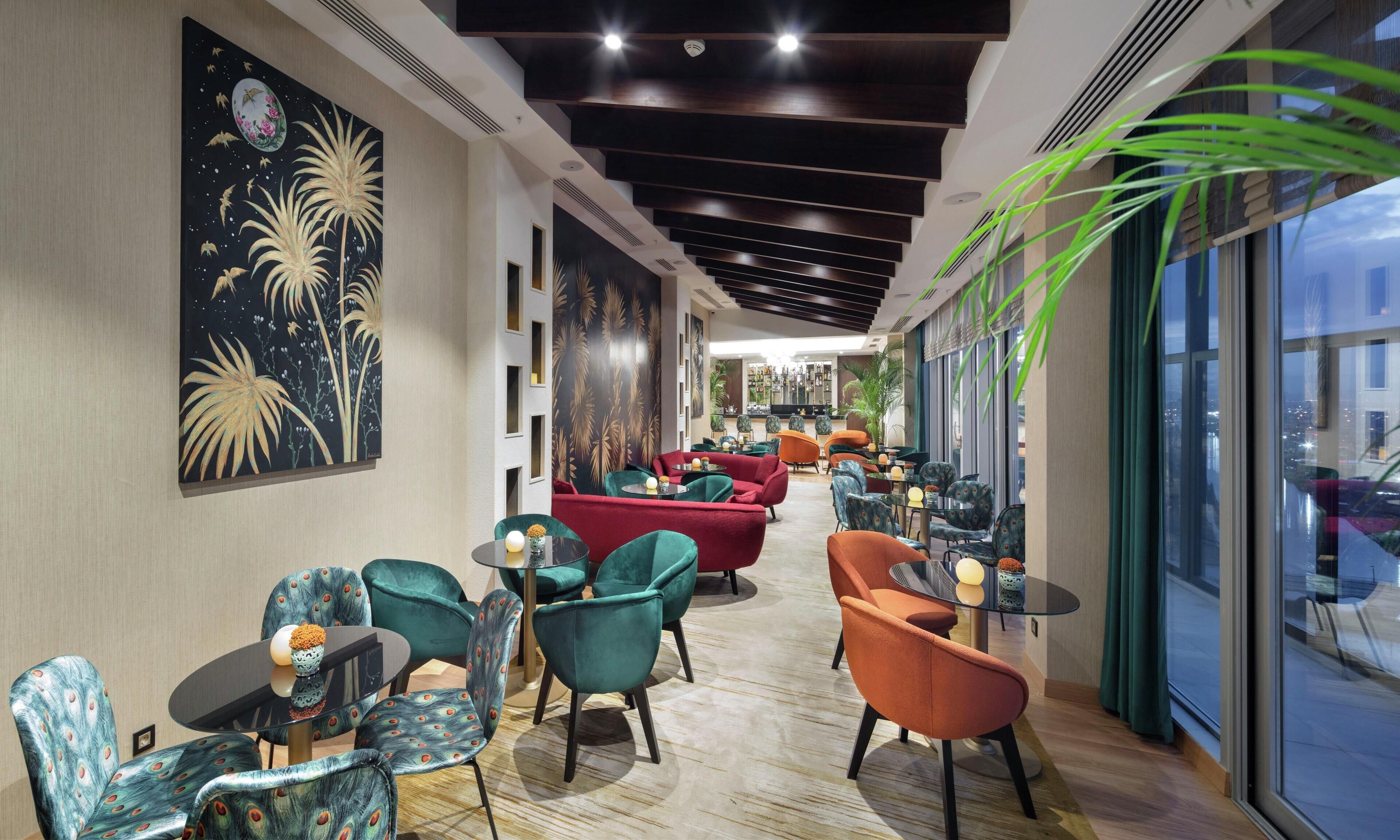 Un hall d’hôtel moderne doté d’un espace salon central, d’une grande fenêtre offrant une vue sur la ville et d’une peinture murale décorative.