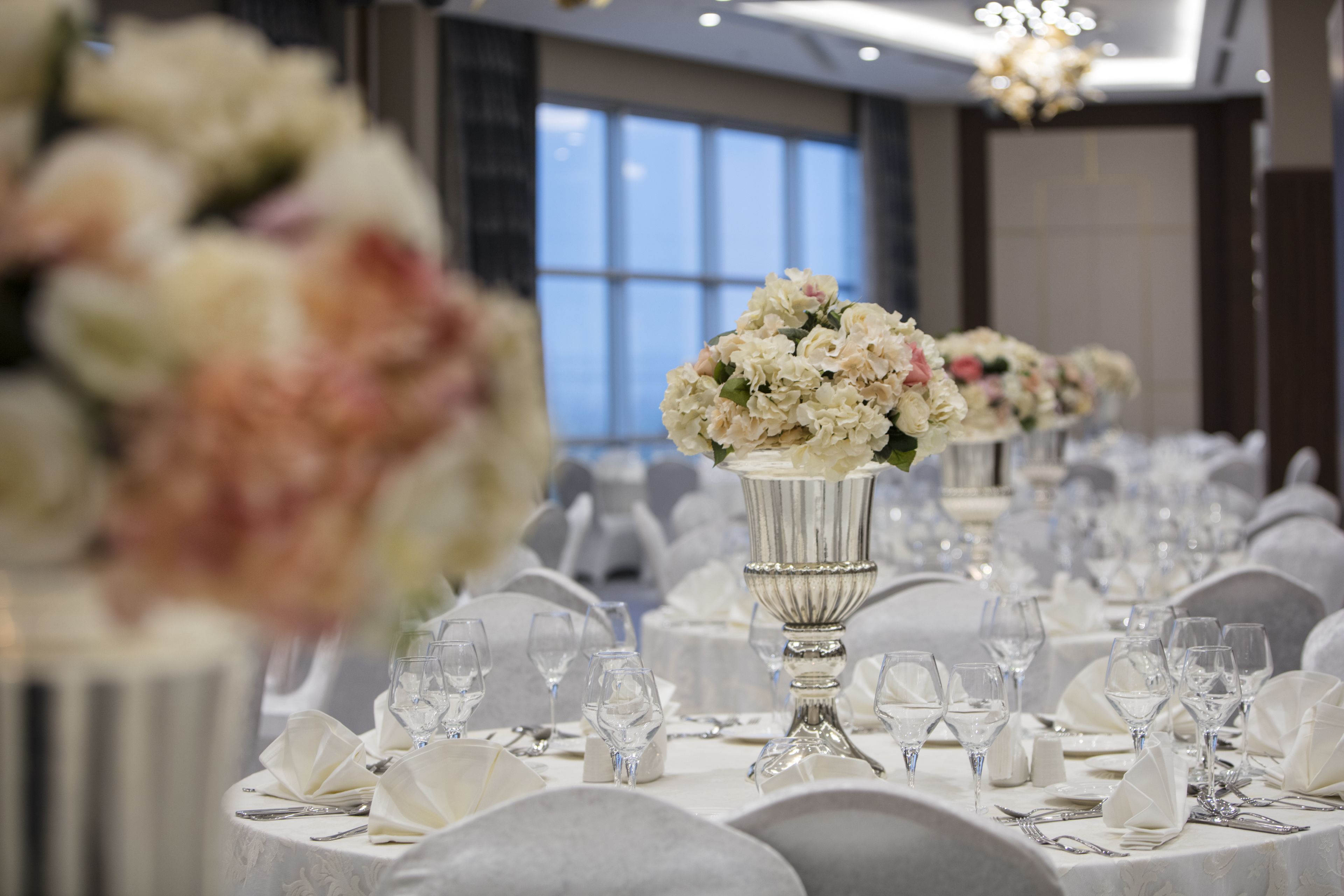 A banquet hall with round tables set for a formal event, featuring white tablecloths and floral centerpieces.