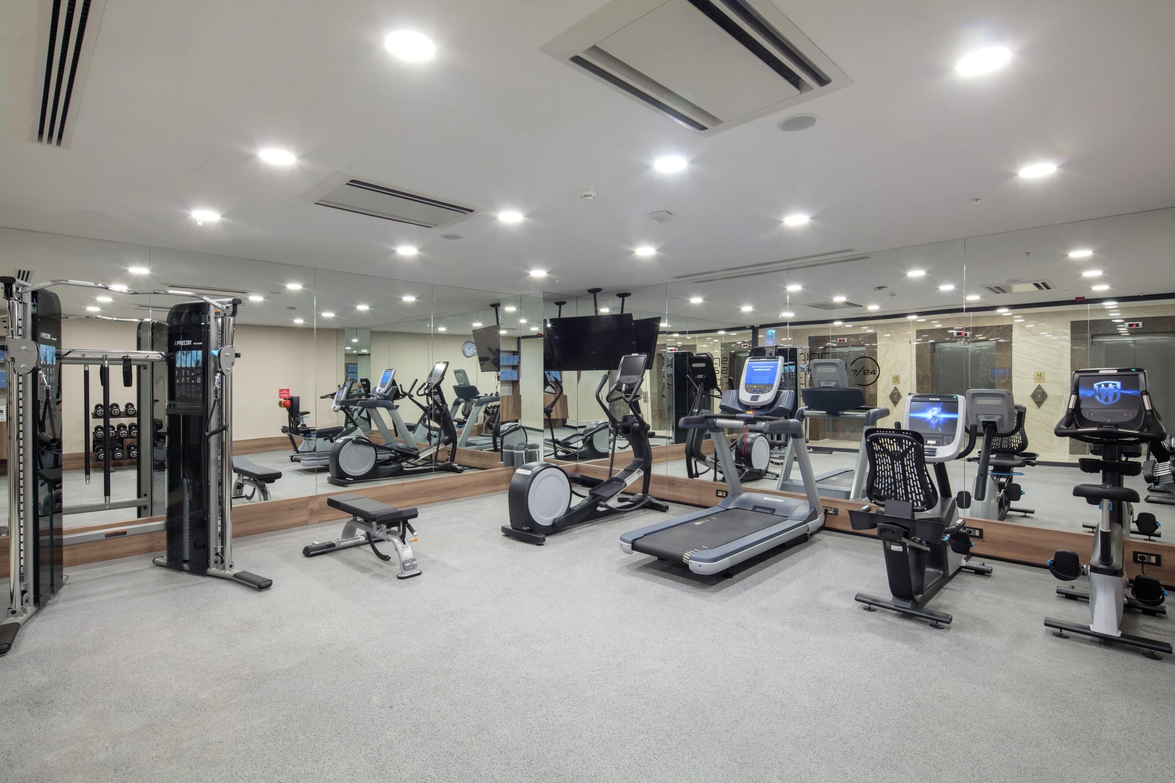 A gym with various exercise equipment, mirrors, and a TV screen.