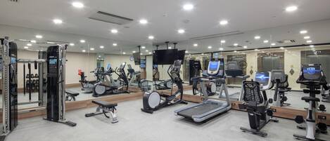 A gym with various exercise equipment, mirrors, and a TV screen.