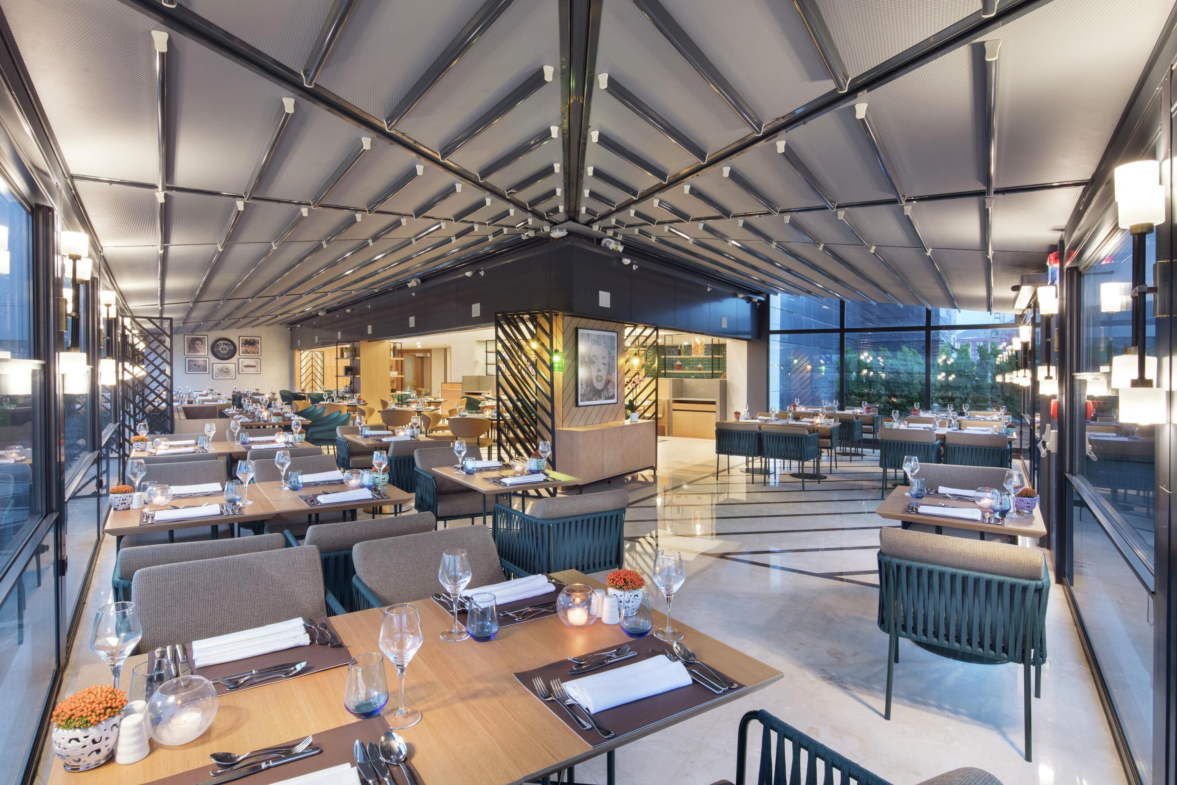 A modern restaurant with multiple dining areas, a central bar, and large windows offering views.