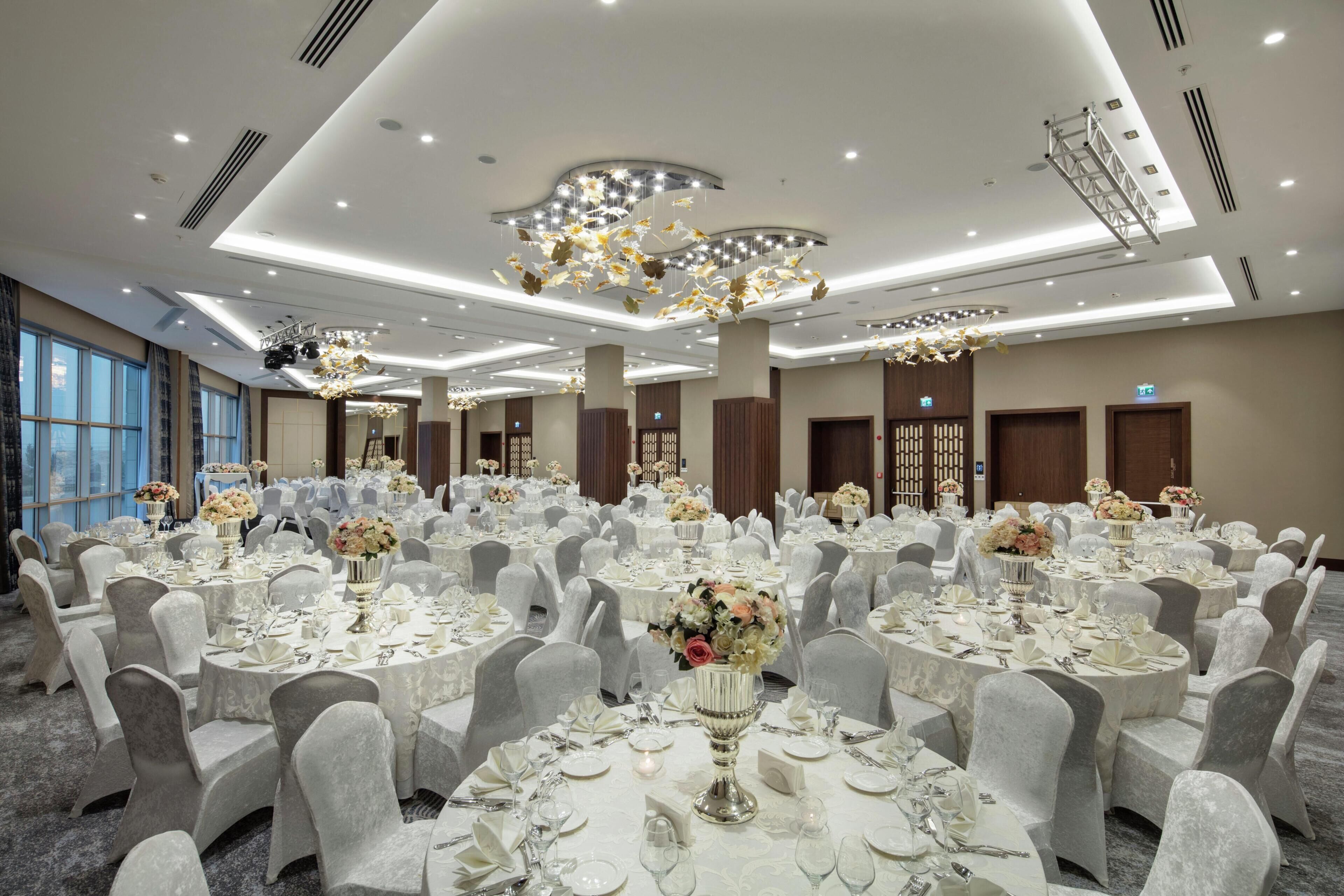 A banquet hall with round tables, white tablecloths, and floral centerpieces.