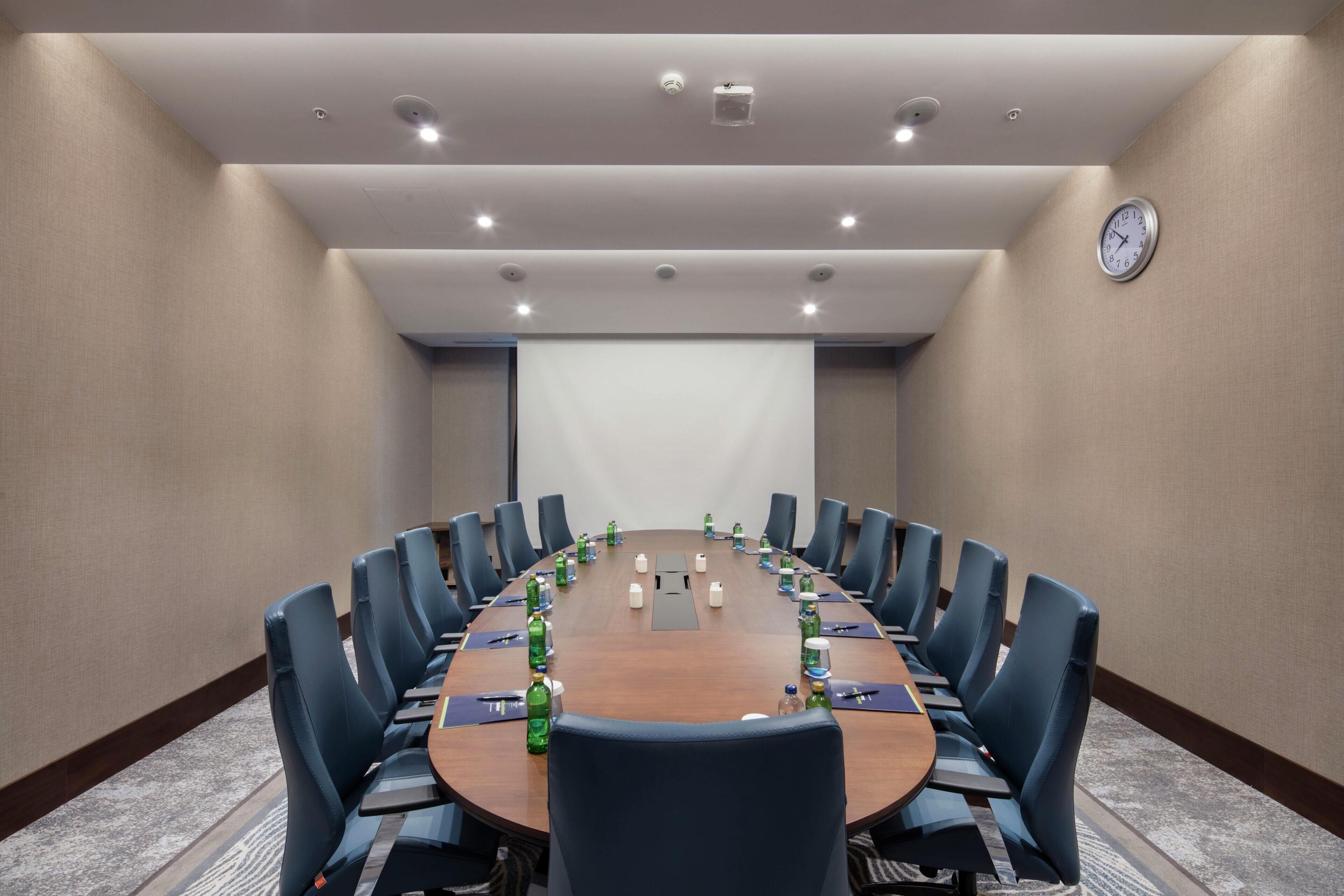 A conference room with a long table, blue chairs, and a clock on the wall.