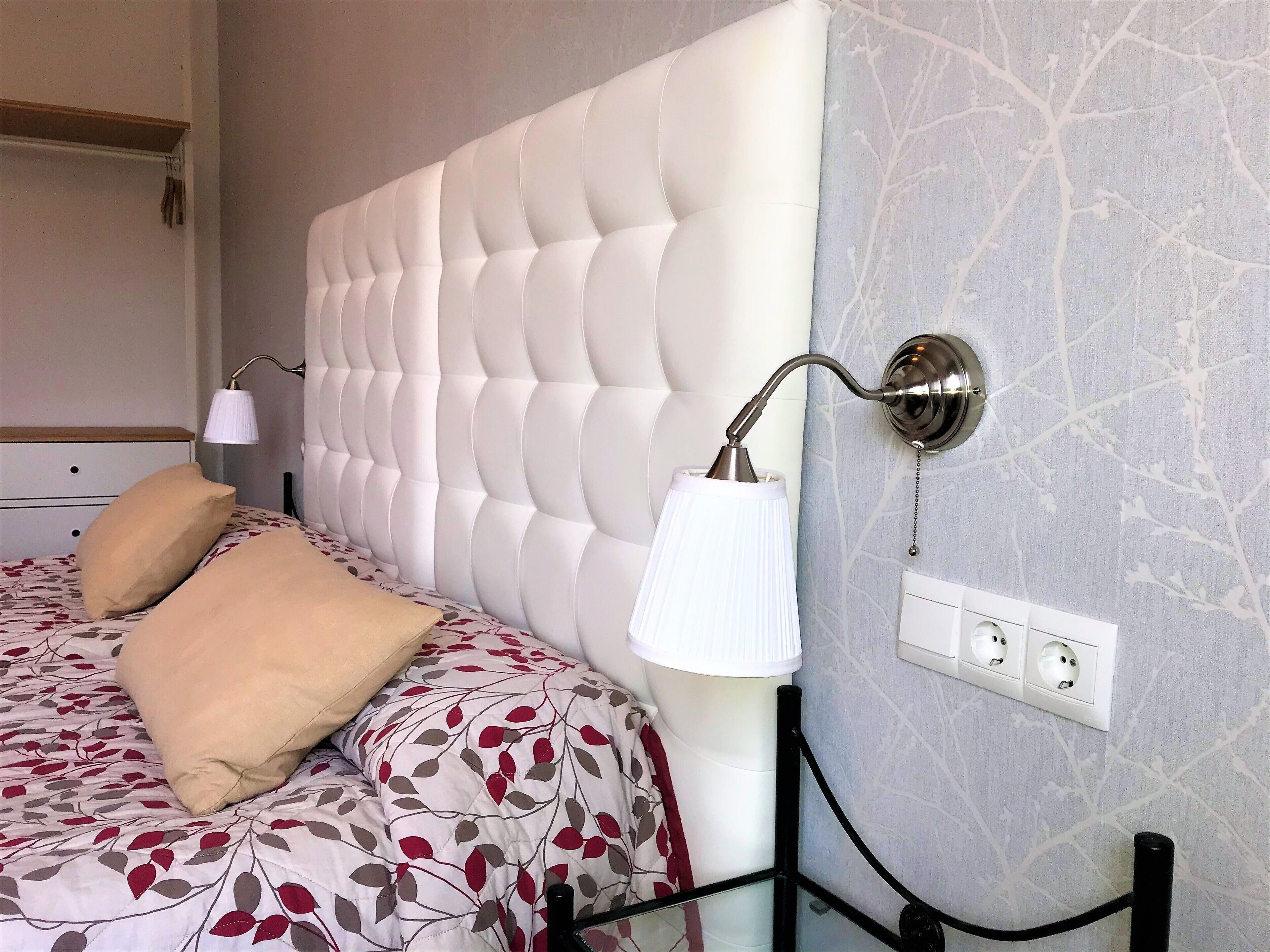 A bedroom with a tufted headboard, a bed with floral bedding, bedside lamps, and a power outlet on the wall.