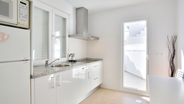 A modern kitchen with white cabinets, a stainless steel range hood, a built-in microwave, and a window overlooking a balcony.