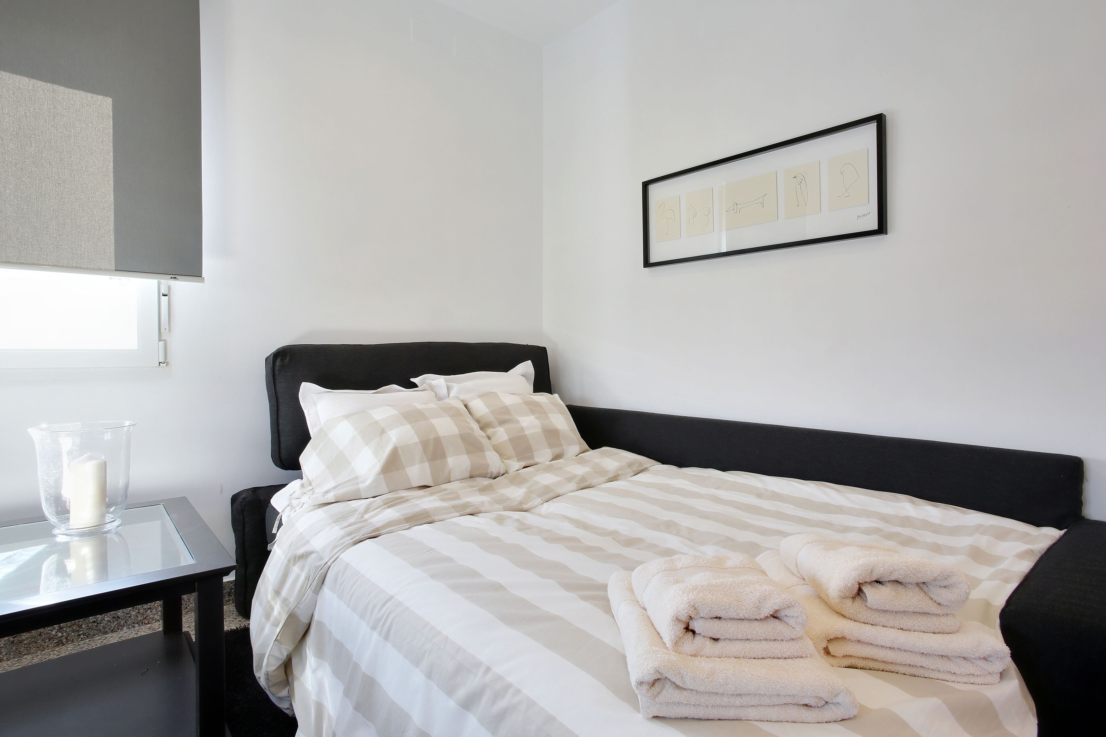 Una cama bien hecha con ropa de cama a rayas, una mesita de noche con una vela y un cuadro en la pared.