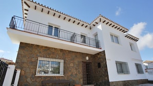 A two-story house with a stone facade, a balcony with black railings, and a tiled roof.