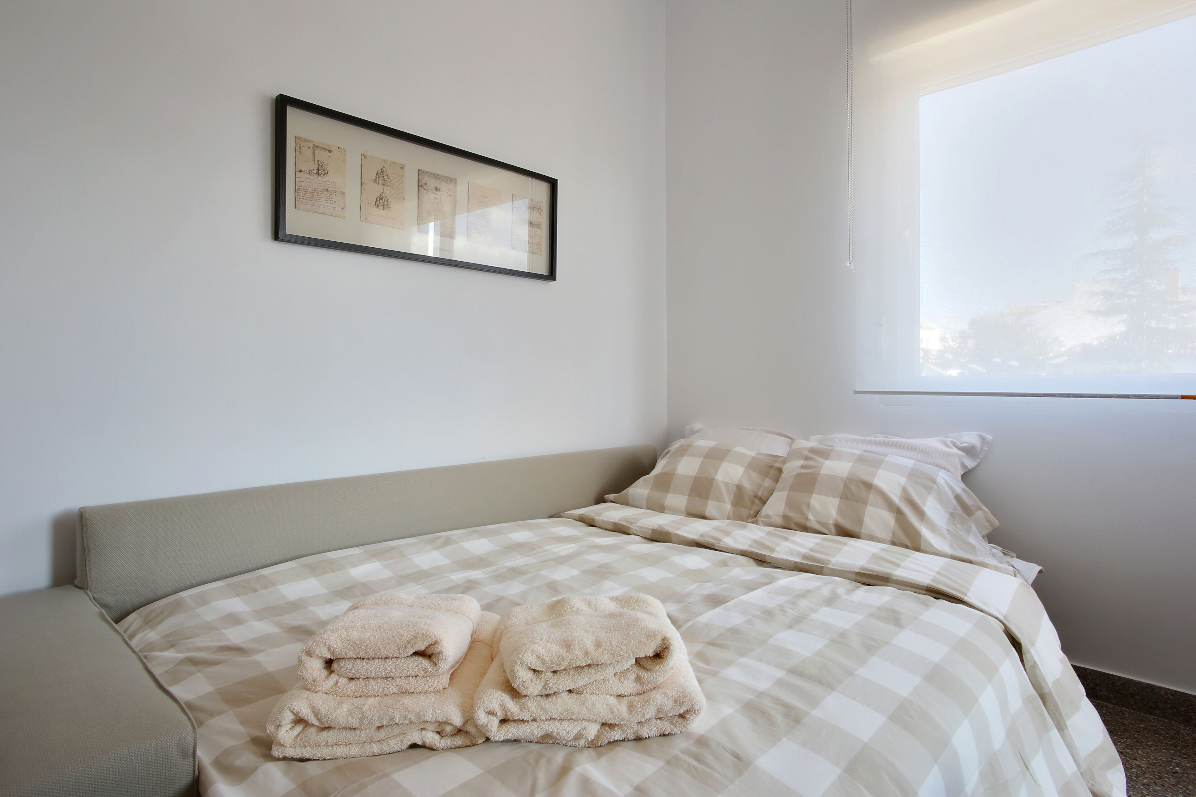 A neatly made bed with checkered bedding, a pair of folded towels, and a framed certificate on the wall.