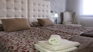 A neatly made bed with a floral bedspread, a headboard, and a rolled towel on the bed.