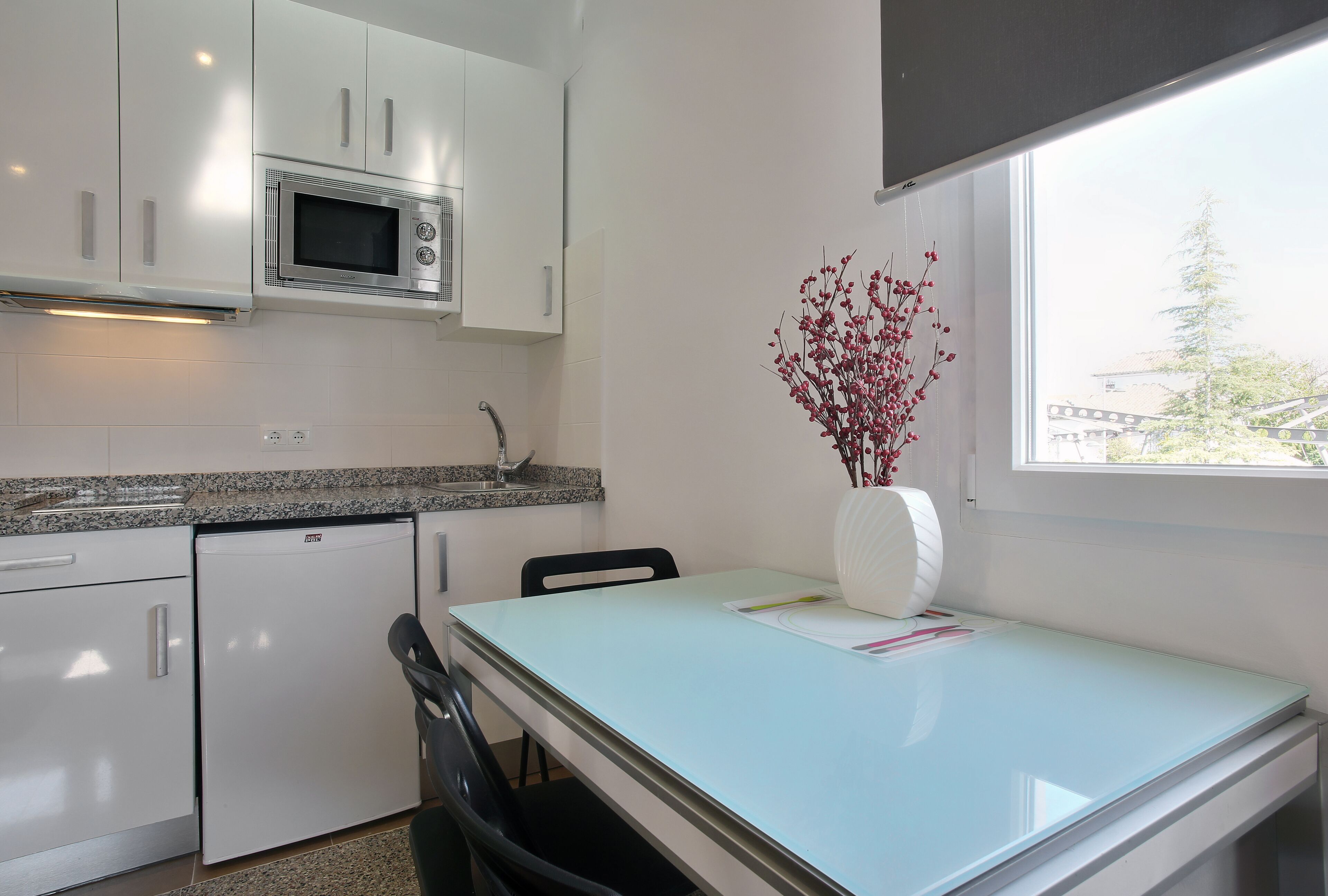Una cocina moderna con armarios blancos, microondas integrado y un comedor con mesa y sillas.
