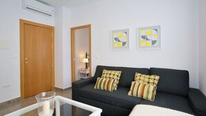 A living room with a sofa, two pillows, a glass coffee table, and a door.