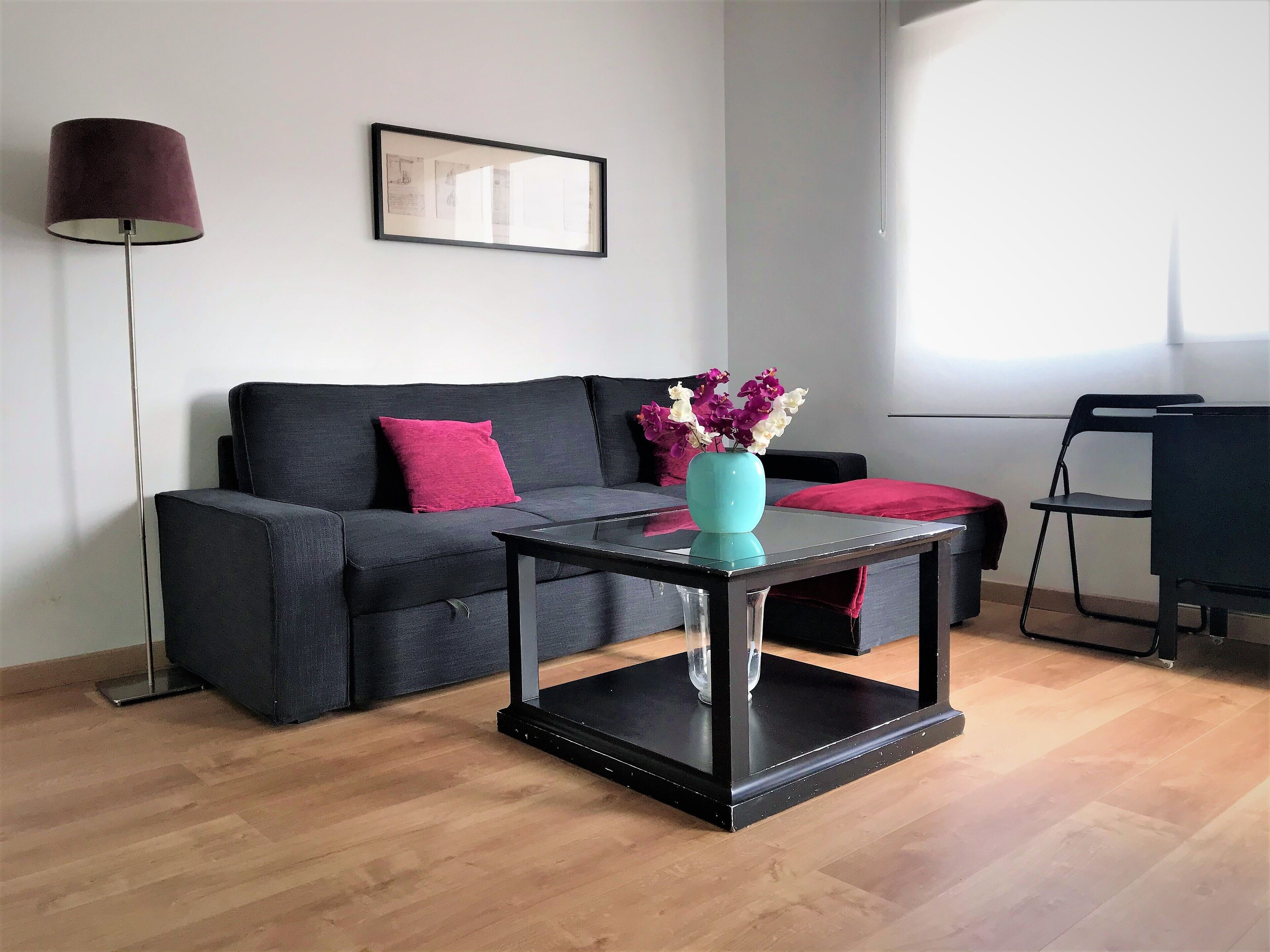 Una sala de estar moderna con un sofá gris oscuro, un florero turquesa con flores y una lámpara de pie negra.