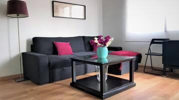 Una sala de estar moderna con un sofá gris oscuro, un florero turquesa con flores y una lámpara de pie negra.