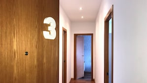 A hallway with wooden flooring, a wooden door with a number '3' sign, and a door leading to another room.