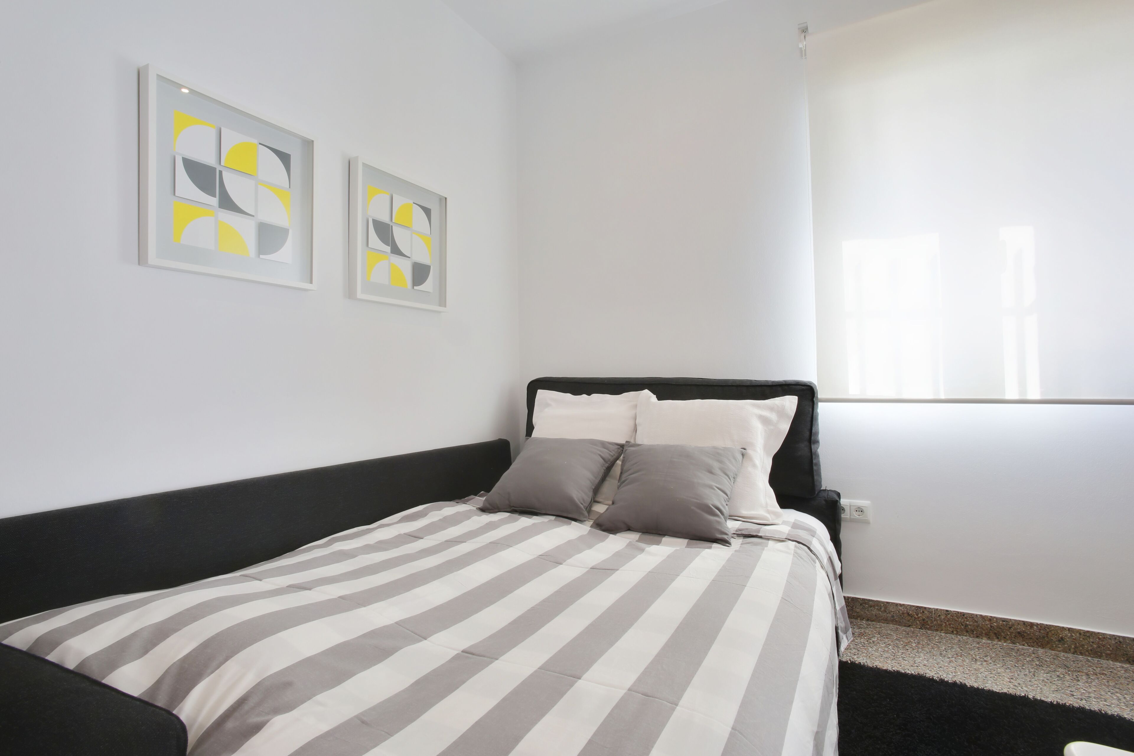 A neatly made bed with striped bedding, a black headboard, and two abstract art pieces on the wall.