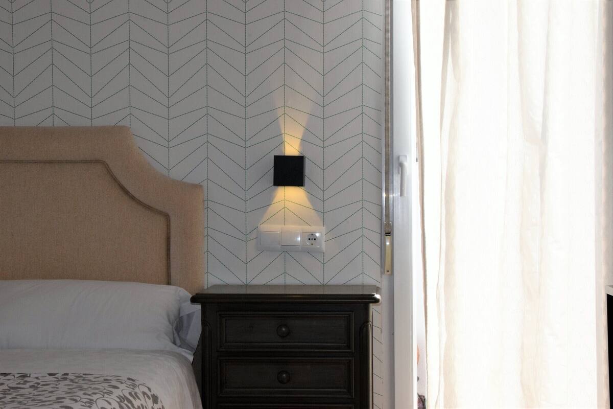 Une chambre à coucher avec un lit, une table de chevet et un luminaire fixé au mur.