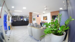 A modern hotel lobby with a reception desk, seating area, and a large potted plant. - Hotel Portal da Amazônia (Varzea Grande)