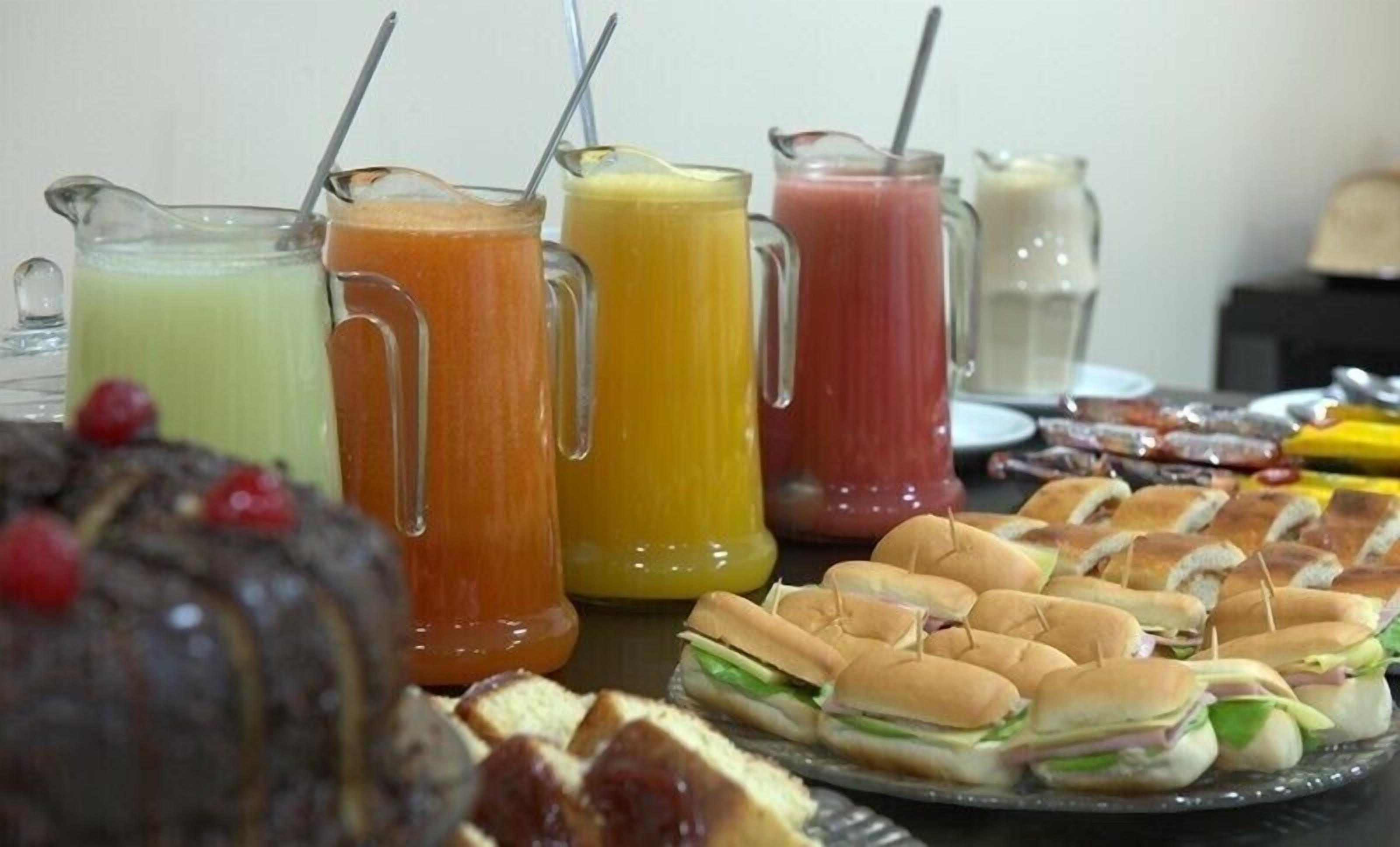 Una mesa de buffet con varios sándwiches y jarras de jugos de frutas.