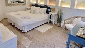 A neatly arranged bedroom with a large bed, bedside tables, a wicker chair, and a small table with items. - Jardines De La Reina Boutique B&B (Marbella)