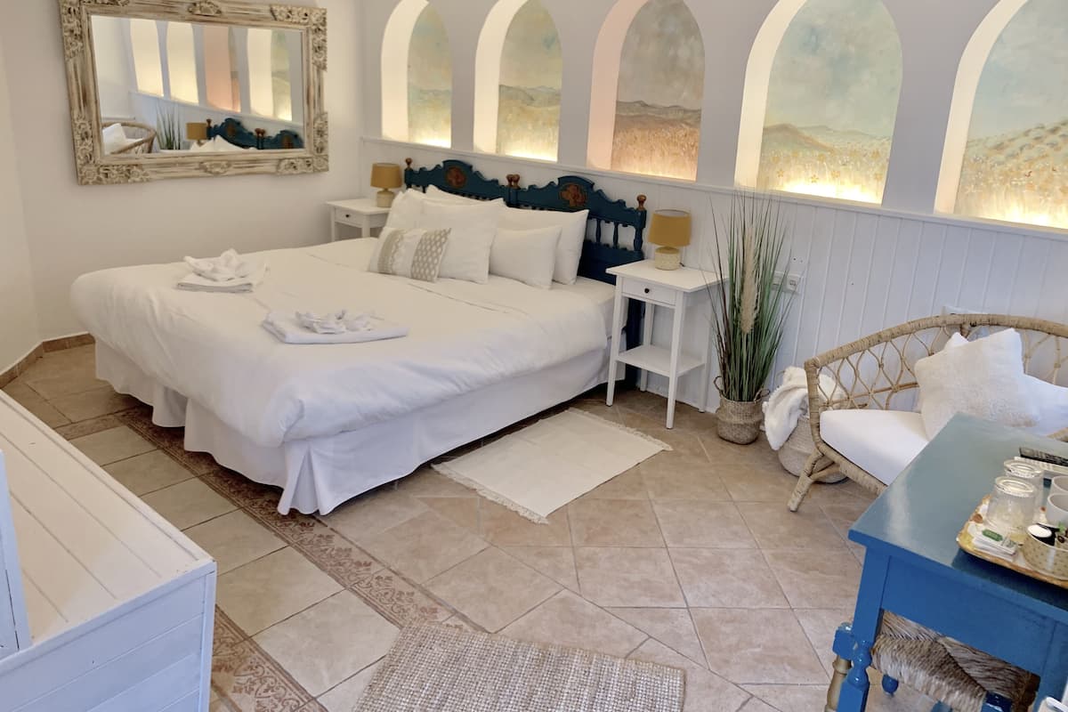 A neatly arranged bedroom with a large bed, bedside tables, a wicker chair, and a small table with items.