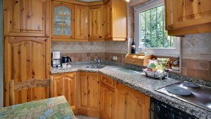A kitchen with wooden cabinets, granite countertops, a built-in oven, and a window with a view of greenery. - Jardines De La Reina Boutique B&B (Marbella)