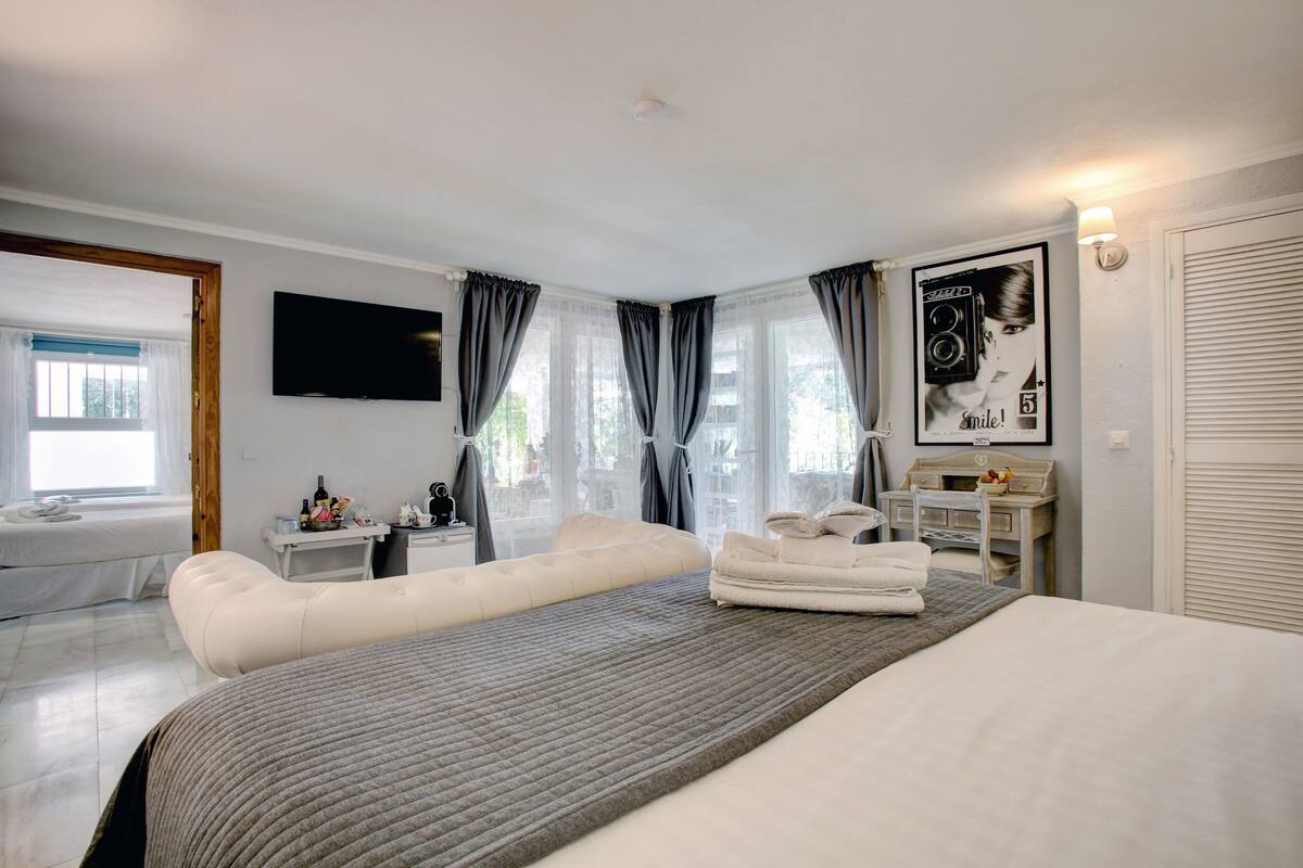 A modern hotel room with a large bed, a bedside table, a desk, and a chair.