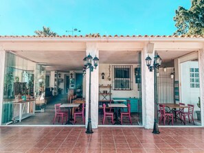 An outdoor patio area with tiled flooring, red chairs, and tables. There are potted plants and a window with barred glass. - Jardines De La Reina Boutique B&B (Marbella)