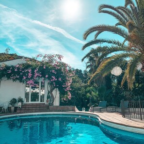 A swimming pool with a clear blue water, surrounded by a garden with pink flowers and palm trees. - Jardines De La Reina Boutique B&B (Marbella)