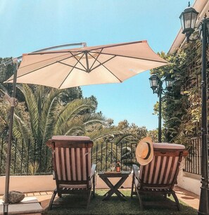 A patio with two wooden chairs, a table, and a large umbrella. - Jardines De La Reina Boutique B&B (Marbella)