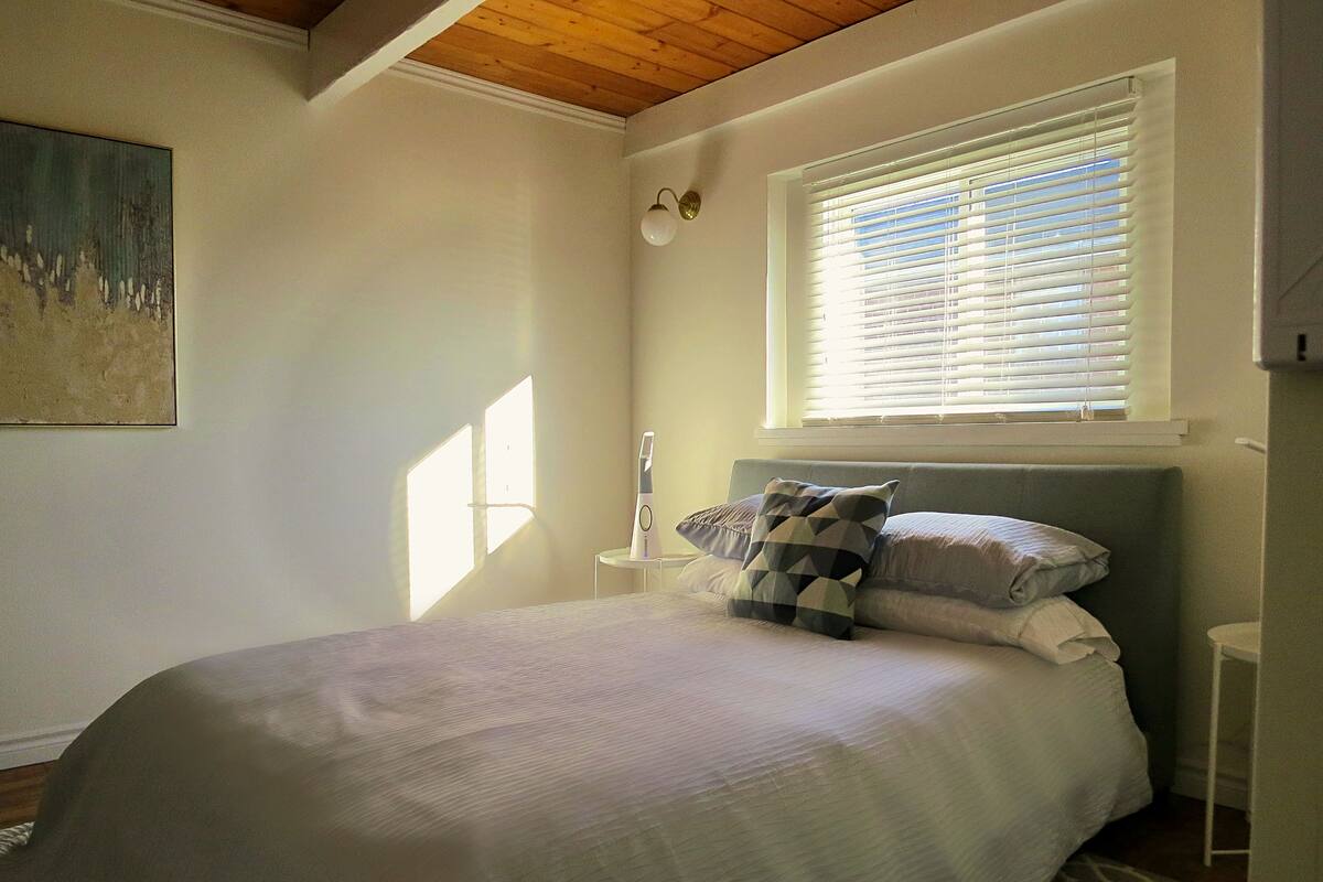 A bedroom with a bed, a nightstand, a lamp, and a window with blinds.