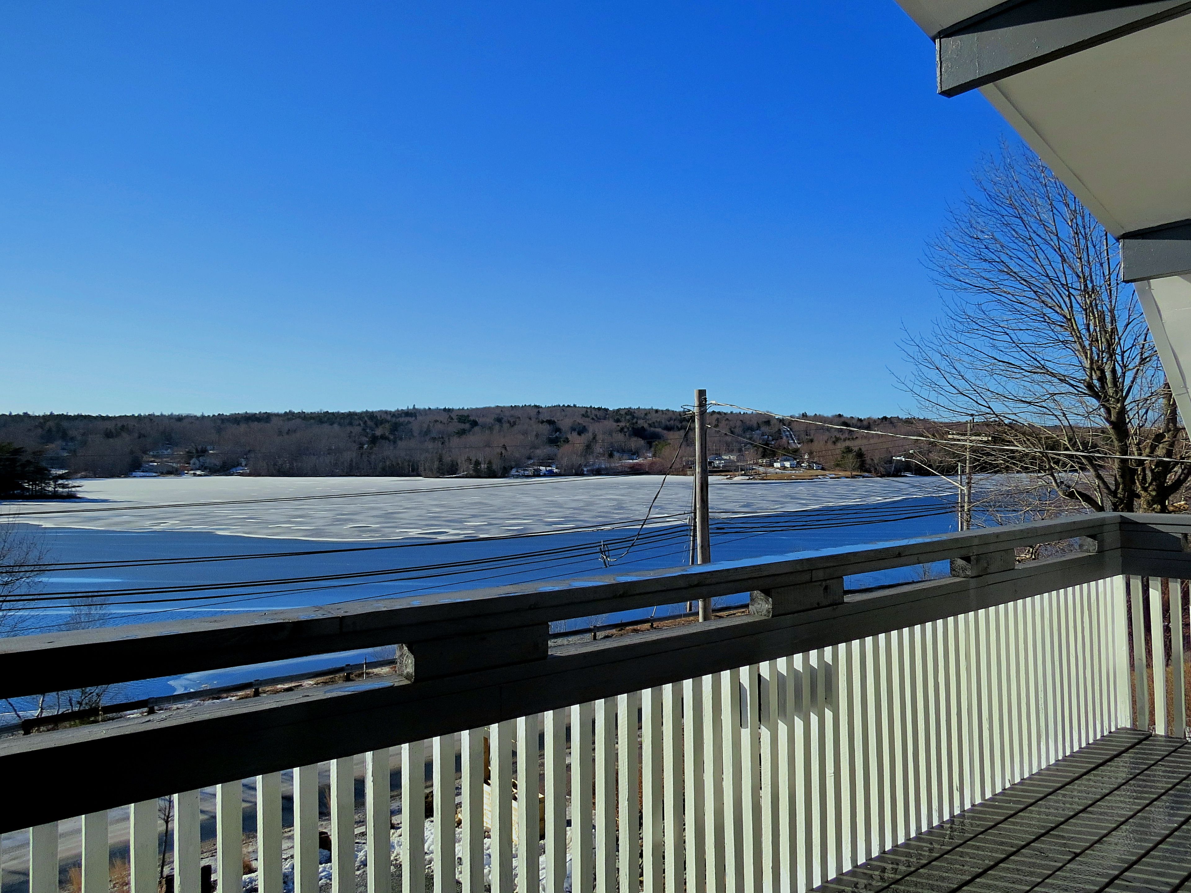 Une vue depuis un balcon doté d’une balustrade en bois, donnant sur un lac gelé et une colline boisée au loin.
