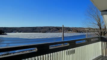 A view from a balcony with a wooden railing, overlooking a frozen lake and a forested hill in the distance.