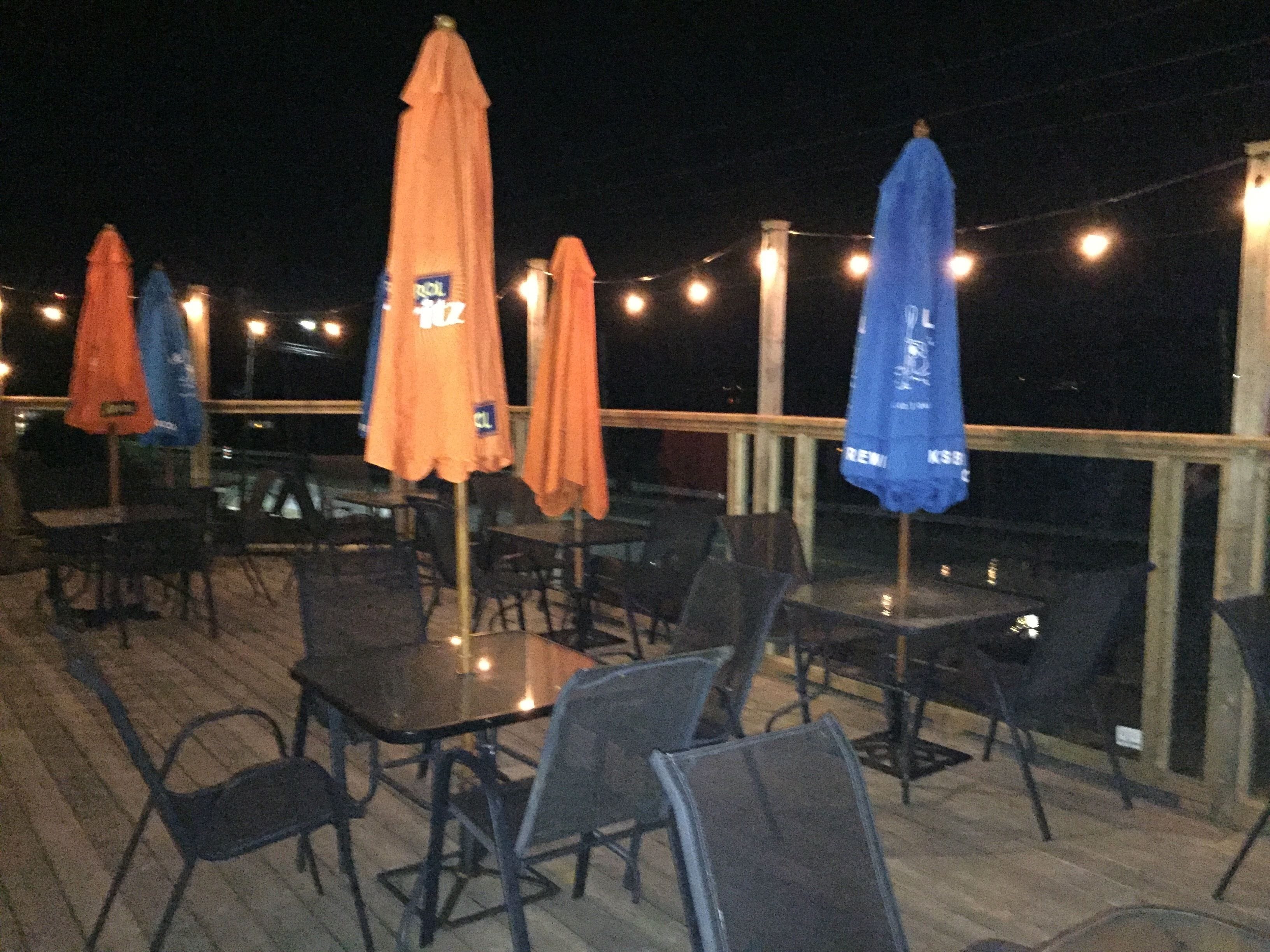 Un espace extérieur aménagé avec des tables, des chaises, des parasols et des guirlandes lumineuses.