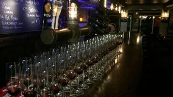 A bar with a long row of wine glasses filled with red wine, a chalkboard menu, and a beer tap.