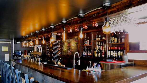 Eine Bar mit einer Holztresen, hängenden Glühbirnen und Regalen voller Spirituosenflaschen.