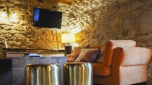 A cozy living room with a stone wall, a flat-screen TV, a sofa, and two metallic stools. - A parada das bestas (Palas de Rei)