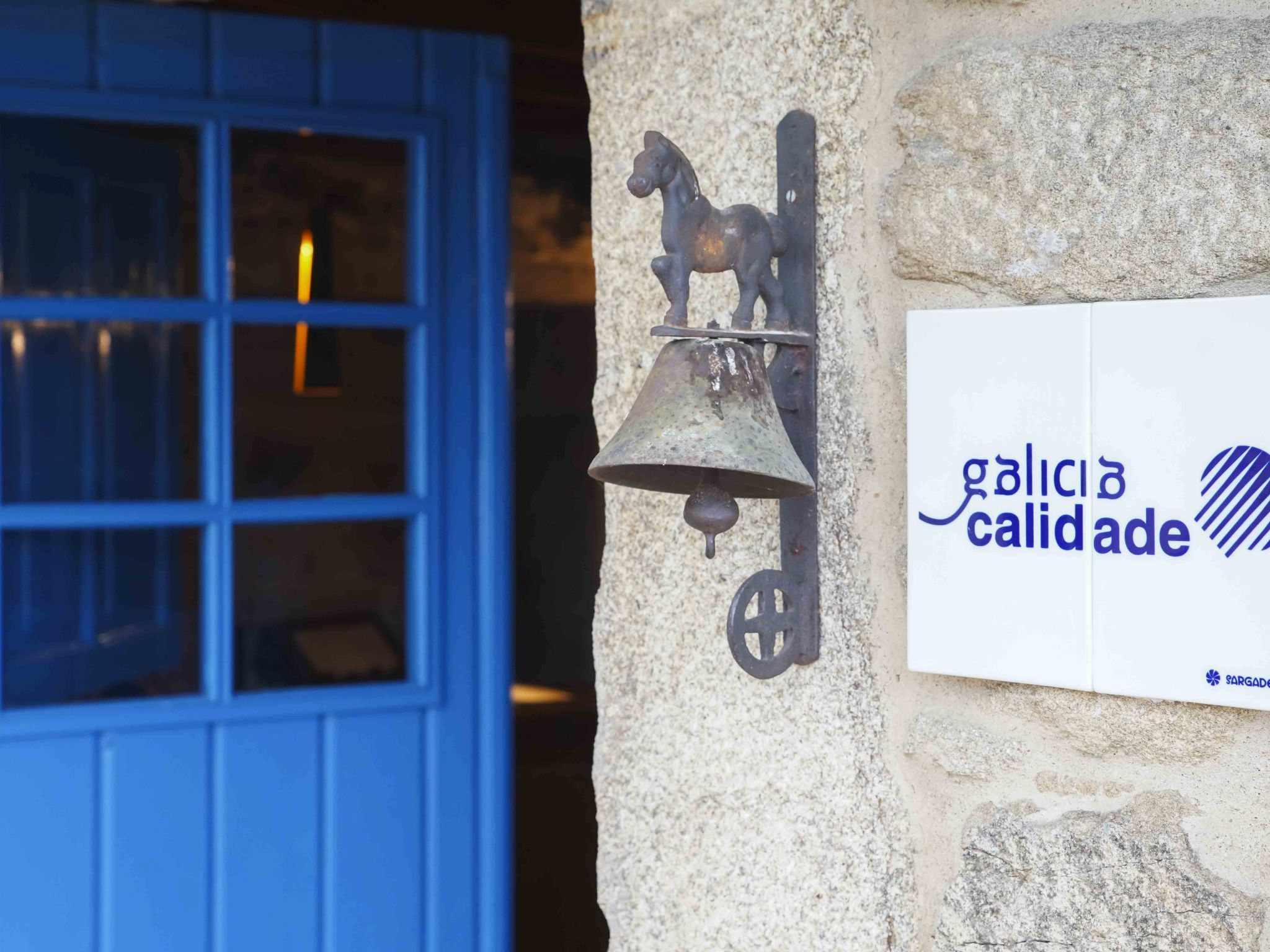 A building entrance with a blue door and a metal bell mounted on a stone wall.