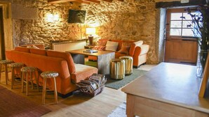 A cozy living room with a stone wall, wooden beams, a sofa, a coffee table, and a TV. - A parada das bestas (Palas de Rei)