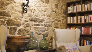 A cozy room with a stone wall, two armchairs, a bookshelf, and decorative vases. - A parada das bestas (Palas de Rei)