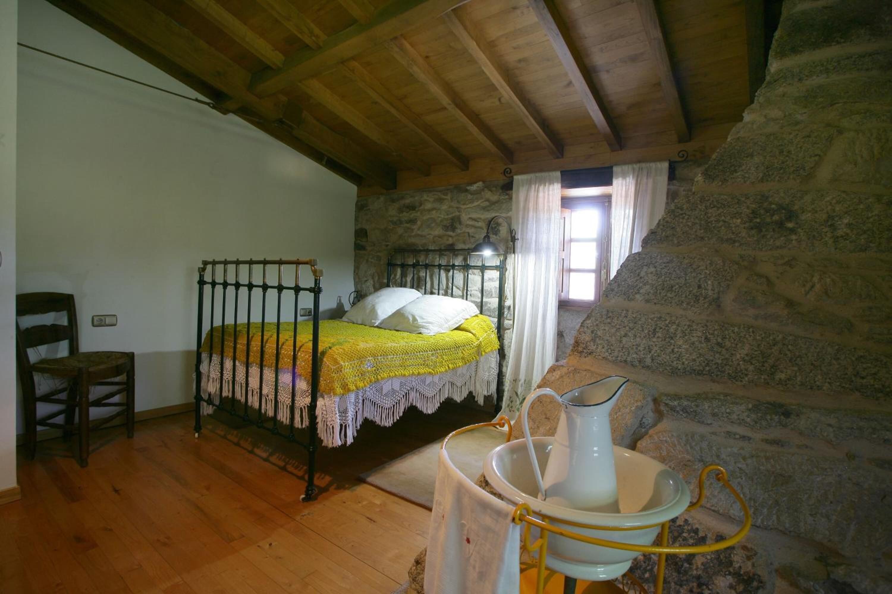 Um quarto rústico com cama de madeira, paredes de pedra, lareira de pedra e um balde de metal.