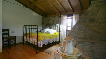 Una habitación rústica con una cama de madera, paredes de piedra, una chimenea de piedra y un cubo de metal.