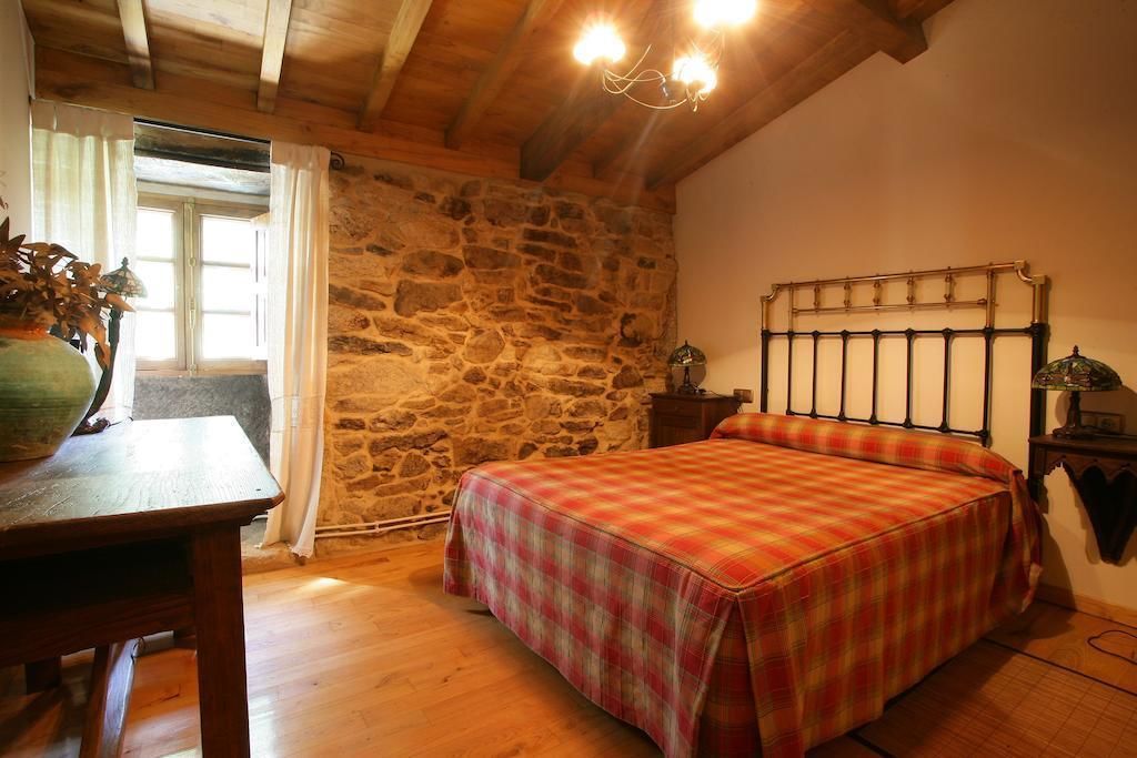Ein Schlafzimmer mit Steinwand, Holzbalkendecke, einem Bett mit kariertem Überwurf, einem Nachttisch mit Lampe und einem Fenster mit Vorhängen.