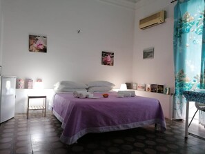 A bedroom with a bed, pillows, a small table, and a chair. There are wall decorations and an air conditioning unit. - A Due Passi B&B (Catania)