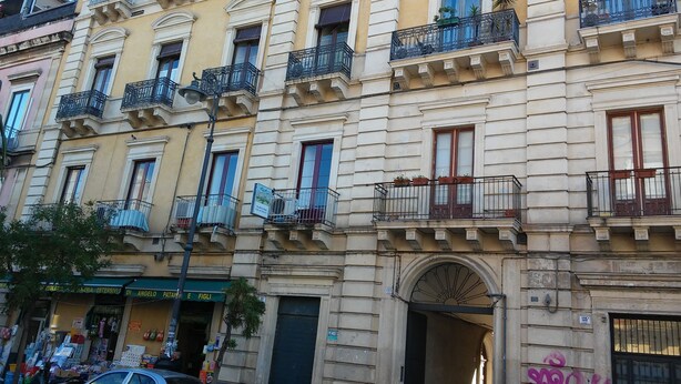 A multi-story building with balconies, a storefront, and a parked car. - A Due Passi B&B (Catania)
