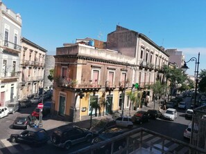 A street view with a building featuring a balcony with potted plants, a visible sign, and parked cars. - A Due Passi B&B (Catania)