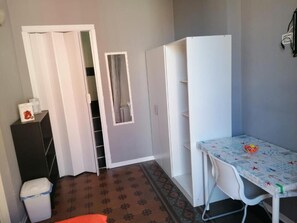 A small room with a white wardrobe, a white table with a patterned tablecloth, and a trash bin. - A Due Passi B&B (Catania)