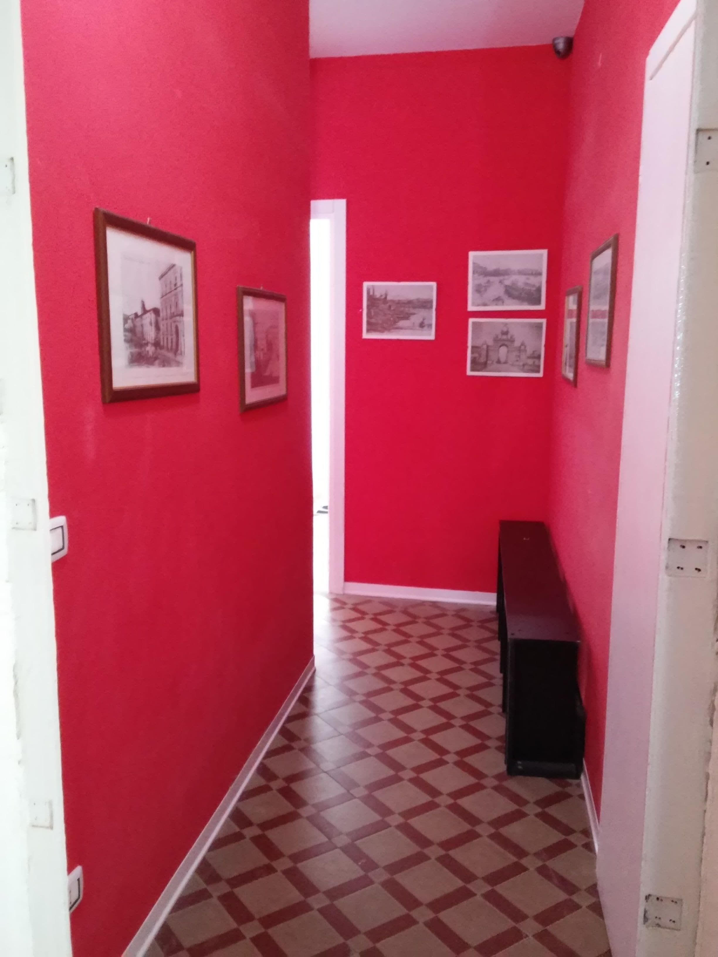 Un pasillo con paredes rojas y piso a cuadros, decorado con varias fotografías enmarcadas.