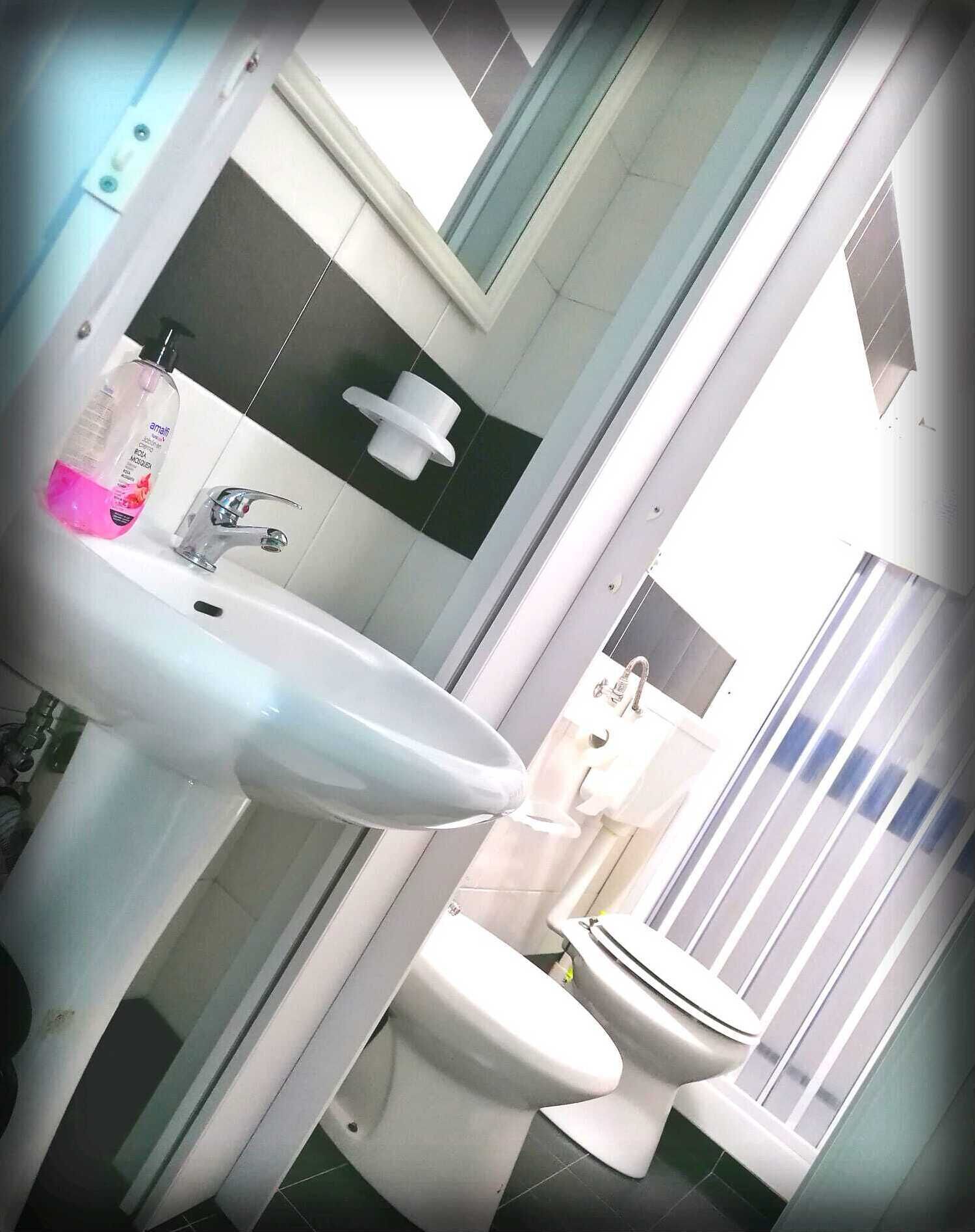 A bathroom with a white sink, a mirror, a toilet, and a shower area.